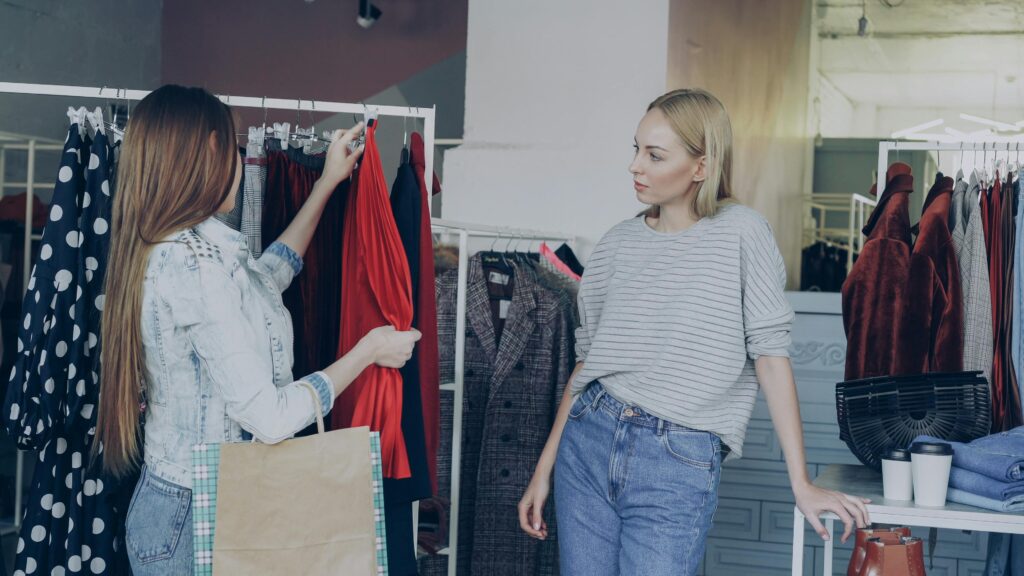 Two women shopping and selecting clothing in a fashion boutique.